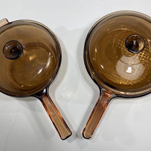 May include: A white ceramic mug with a black handle and the text "But First, Coffee" in a bold, black font. The mug is set against a blurred background, highlighting its clean design. The mug appears to be 10 cm tall.