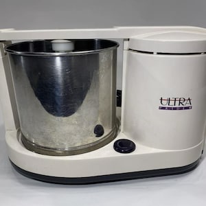 May include: White electric food grinder with a stainless steel bowl. The grinder has a purple button and says "Ultra Pride" on the side.
