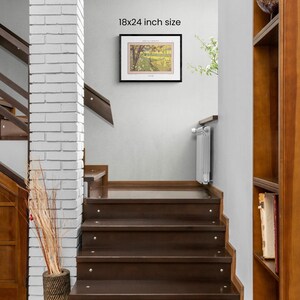 May include: A framed print of a landscape painting with a black frame. The print is 18x24 inches and is hanging on a white wall in a home.