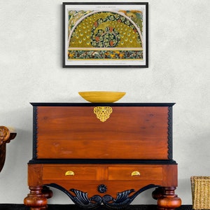 Puede incluir: Una ilustraci&oacute;n vintage de un dise&ntilde;o de pavo real con una combinaci&oacute;n de colores verde, amarillo y marr&oacute;n. La ilustraci&oacute;n est&aacute; enmarcada y se muestra en una pared sobre un cofre de madera con dos cajones. El cofre tiene una base negra y detalles dorados.