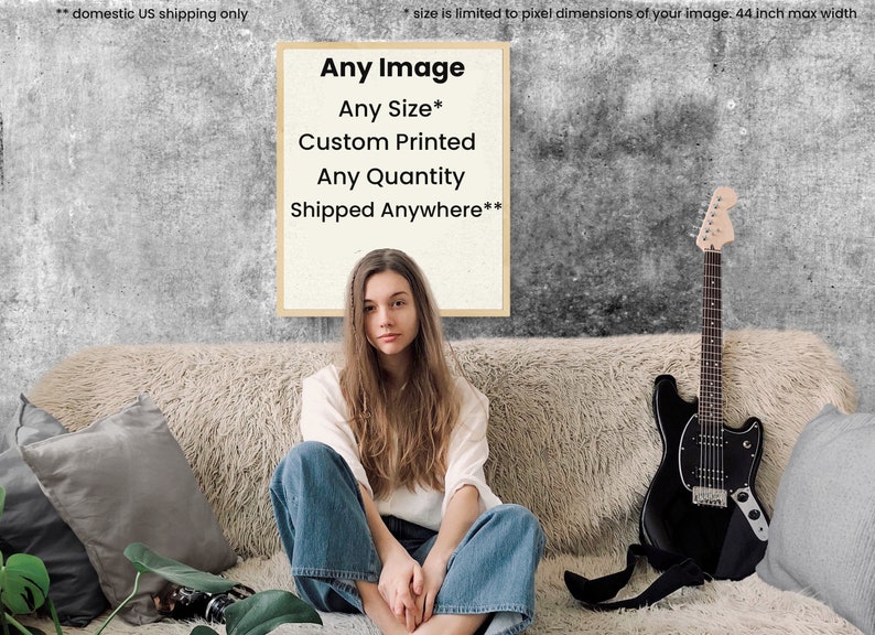 May include: A framed poster with the text "Any Image", "Any Size*", "Custom Printed", "Any Quantity", and "Shipped Anywhere**" on a white background. The poster is hanging on a gray wall behind a couch with a woman sitting on it. A black electric guitar is leaning against the couch.