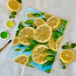 Puede incluir: Una pintura a la acuarela con rodajas de lim&oacute;n y hojas verdes sobre un fondo azul claro. Medias rodajas de lim&oacute;n fresco y ramitas de menta est&aacute;n dispuestas alrededor de la pintura. Tambi&eacute;n se ven pinturas de acuarela y un pincel.
