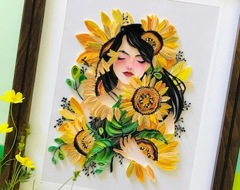 Puede incluir: Obra de arte en quilling enmarcada que representa a una mujer rodeada de girasoles. La obra utiliza papel amarillo, naranja, verde y negro. El marco es de madera marrón oscuro.