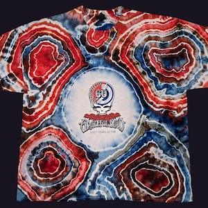 May include: A tie-dye t-shirt with a red, white, and blue swirl pattern. The shirt features a circular logo with the text "Grateful Dead" and "Sixty Years So Far".