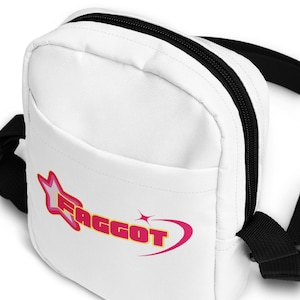 Peut inclure: Sac bandoulière en toile blanche avec une bandoulière réglable noire. Le sac a une poche avant avec un motif rose et jaune qui dit "FAGGOT" avec une étoile et une ligne courbe.