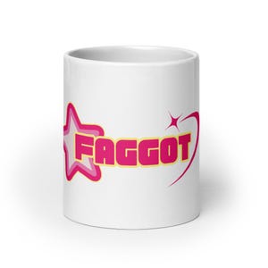 May include: White ceramic mug with a pink star and the word "FAGGOT" in yellow letters.
