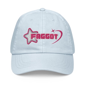 May include: Light blue baseball cap with embroidered text "FAGGOT" in pink and white, accompanied by a star and swoosh design. The cap features a curved brim and an adjustable strap at the back.