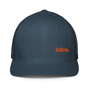 Op de afbeelding: Een donkerblauwe truckercap met een mesh achterkant en een oranje geborduurd logo met de tekst "btm."