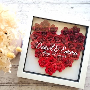 May include: A white shadow box containing a red paper flower heart. The heart is made of many small red paper roses. The text "Daniel & Emma Always and Forever" is written in white on the front of the box.