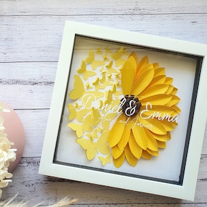 May include: A framed paper artwork depicting a yellow sunflower with butterfly details. The names "Daniel & Emma" and the phrase "Always and Forever" are inscribed in white script. The frame is white.