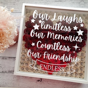 May include: A framed piece of art with a heart made of red and beige paper roses. White text reads "Our Laughs limitless Our Memories Countless Our Friendship Endless". The frame is white.