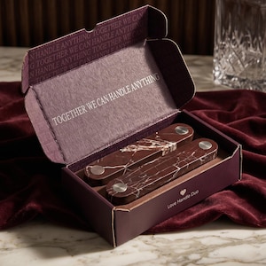 May include: A dark purple cardboard box containing two rectangular, dark red marble-patterned handles with silver-tone metal hardware. The interior lid features the text TOGETHER WE CAN HANDLE ANYTHING, and the box exterior reads Love Handle Duo.