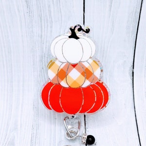 May include: A white, orange, and red plaid pumpkin stack badge reel with a black bead and a clear crystal charm.