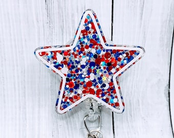 May include: A red, white, and blue glitter star-shaped badge holder with a silver retractable reel and a silver charm with glitter. The charm is attached to a clear plastic badge holder with a red and blue beaded chain.
