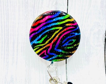 Peut inclure: Un porte-badge rétractable noir avec un motif zèbre arc-en-ciel. Le porte-badge est doté d'un clip pivotant argenté et d'une perle noire.