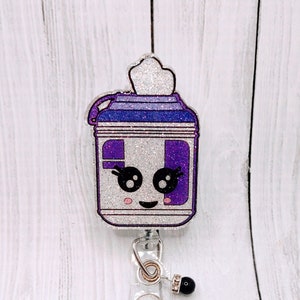 May include: A white and purple glitter badge reel with a cartoon tissue box design. The tissue box has a white lid and a purple body with a white face and black eyes. The reel has a black bead and a clear plastic holder.