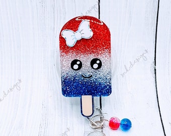 Peut inclure: Breloque en forme de popsicle rouge, blanc et bleu avec des paillettes, un nœud blanc et un visage mignon. Le charme est attaché à un porte-badge rétractable avec un clip pivotant argenté et une perle rouge et bleue.