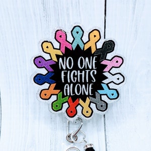 May include: A clear badge reel with a silver charm and a black bead. The badge reel features a colorful circle of awareness ribbons with the text "NO ONE FIGHTS ALONE" in black and white.