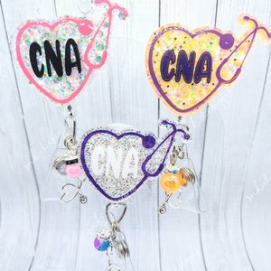 Peut inclure: Trois porte-badges en forme de c&oelig;ur avec des paillettes et le texte "CNA" sur chacun. Les porte-badges sont attach&eacute;s &agrave; des enrouleurs de badge r&eacute;tractables avec diff&eacute;rents breloques.