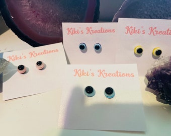 May include: Four pairs of small, colorful eye-shaped earrings on white cards with the text "Kiki's Kreations".