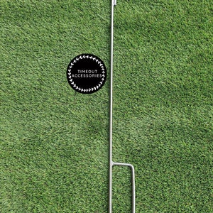 May include: A silver metal tent pole with a hook at the top and a loop at the bottom. The pole is on a green artificial grass background. The text "TIMEOUT ACCESSORIES" is on a black circle with a wreath around it.