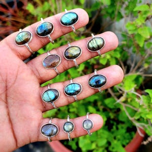 May include: A collection of silver rings with oval-shaped labradorite gemstones. The rings are displayed on a hand, showcasing the iridescent colors of the stones.