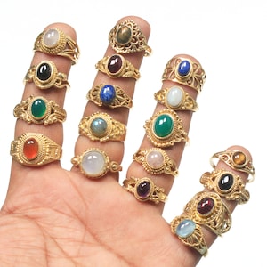 Könnte beinhalten: Eine Sammlung von 14 goldenen Ringen mit verschiedenen Edelsteineinsätzen. Die Ringe zeigen verschiedene farbige Edelsteine, darunter Grün, Rot, Blau, Schwarz und Weiß. Die Ringe sind alle aus Gold gefertigt und haben komplizierte Designs.