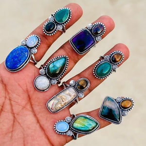 Könnte beinhalten: Eine Sammlung von neun Silberringen mit verschiedenen Edelsteinbesatzungen. Die Ringe zeigen eine Vielzahl von Steinen, darunter Amethyst, Lapislazuli, Labradorit, Tigerauge und Mondstein. Die Ringe sind alle einzigartig und haben einen Boho-Stil.