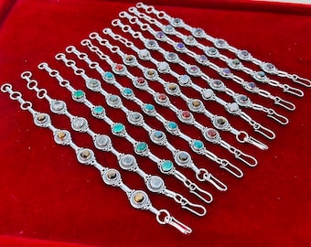Op de afbeelding: Een set van 14 zilveren armbanden met verschillende gekleurde edelstenen. Elke armband heeft een sluiting.
