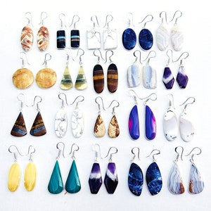 Puede incluir: Un conjunto de 20 pares de pendientes colgantes con diferentes piedras semipreciosas, incluyendo ágata, ojo de tigre y amatista. Los pendientes son plateados y tienen una variedad de formas y colores.