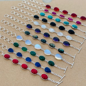 May include: A set of 10 silver chain bracelets with teardrop-shaped gemstone charms. The charms are in various colors, including red, pink, turquoise, black, white, purple, green, and blue.