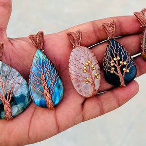 May include: Five wire-wrapped tree of life pendants with different colored stones. The stones are labradorite, rose quartz, black onyx, and red jasper. The pendants are made with copper wire and have gold beads for the leaves.