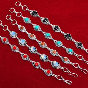 Op de afbeelding: Zes zilveren armbanden met verschillende gekleurde edelstenen. De armbanden hebben een haakgesp en zijn gemaakt van zilver met een decoratief ontwerp. De edelstenen zijn rood, turquoise, bruin en wit.