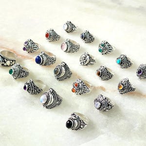 Puede incluir: Una colección de anillos de plata con piedras preciosas de varios colores. Cada anillo presenta diseños intrincados y un pequeño compartimento que se puede abrir.
