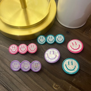 May include: Assortment of colorful smiley face hair clips. The clips are made of a pearly white material with a colorful outline. The colors include pink, purple, teal, and turquoise.