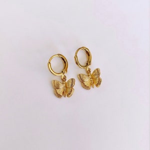 May include: A pair of gold hoop earrings with a dangling butterfly charm. The butterfly charm is detailed with textured wings.