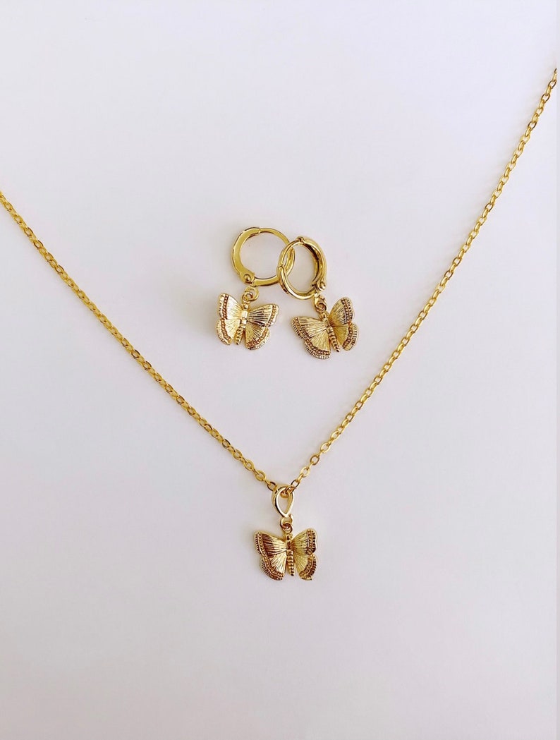 May include: A gold necklace and earrings set featuring a delicate butterfly pendant and matching butterfly hoop earrings.