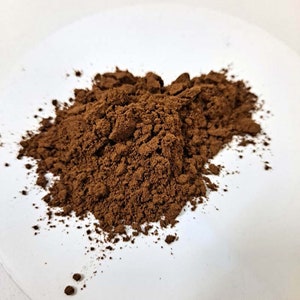 Può includere: Primo piano di un mucchio di polvere di cacao marrone su una superficie bianca.