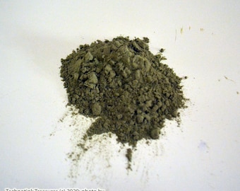 May include: A pile of loose, green powder on a white surface.