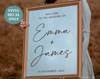 May include: A white wedding sign with a gold frame. The sign says "Welcome to the wedding of Emma + James" and "25 November 2023".
