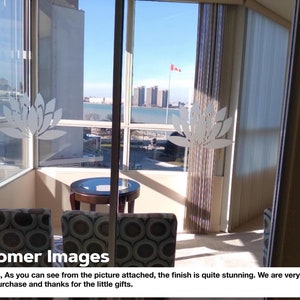 May include: A view from a high-rise apartment with floor-to-ceiling windows overlooking a city skyline and a body of water. The windows have decorative white lotus flower decals. Two chairs with patterned fabric are positioned in front of a small round table.