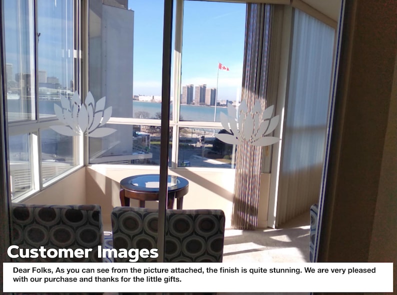 May include: A view from a high-rise apartment with floor-to-ceiling windows overlooking a city skyline and a body of water. The windows have decorative white lotus flower decals. Two chairs with patterned fabric are positioned in front of a small round table.