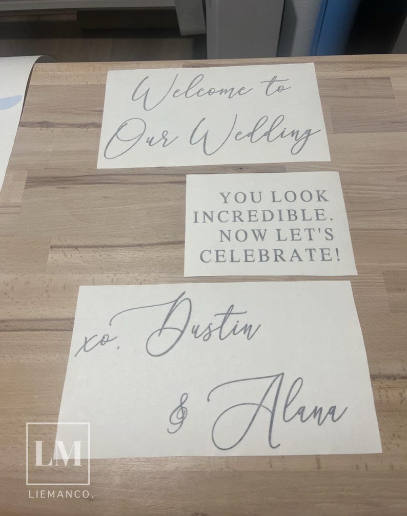 Op de afbeelding: Drie witte rechthoekige vinylstickers met grijze letters. De bovenste sticker bevat de tekst Welcome to Our Wedding in cursief schrift. De middelste sticker bevat YOU LOOK INCREDIBLE. NOW LET'S CELEBRATE! in blokletters. De onderste sticker bevat xo. Dustin & Alana.