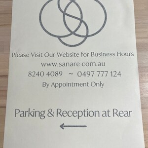K&ouml;nnte beinhalten: Ein wei&szlig;es Schild mit einem grauen Logo aus drei sich &uuml;berlappenden Kreisen. Das Schild enth&auml;lt den Text "Please Visit Our Website for Business Hours", "www.sanare com.au", "8240 4089 ~ 0497 777 124", "By Appointment Only", "Parking & Reception at Rear" und "@sanare_wellness".