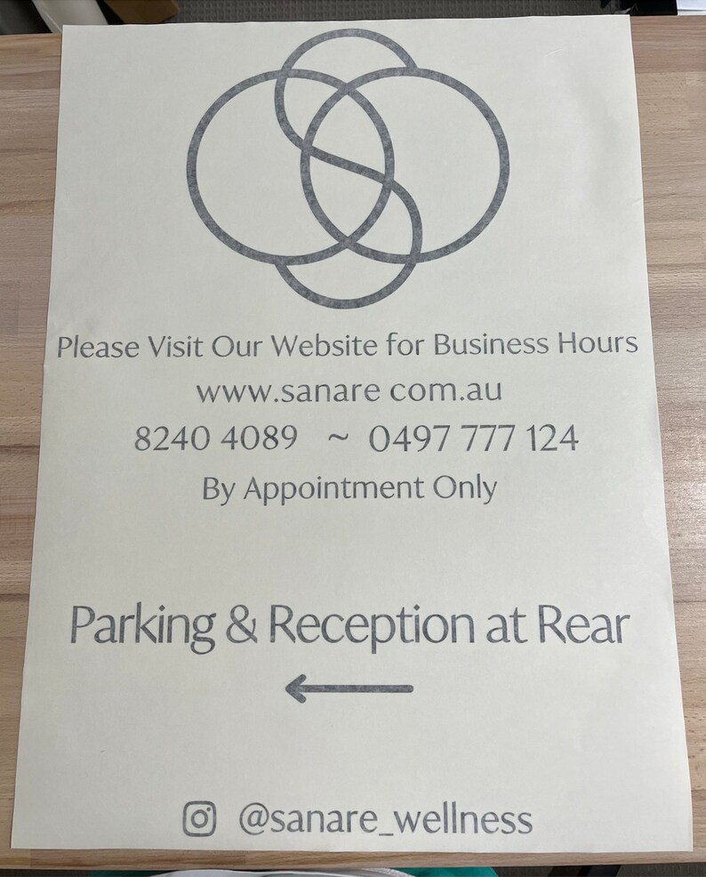 K&ouml;nnte beinhalten: Ein wei&szlig;es Schild mit einem grauen Logo aus drei sich &uuml;berlappenden Kreisen. Das Schild enth&auml;lt den Text "Please Visit Our Website for Business Hours", "www.sanare com.au", "8240 4089 ~ 0497 777 124", "By Appointment Only", "Parking & Reception at Rear" und "@sanare_wellness".