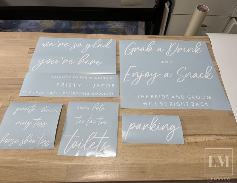 K&ouml;nnte beinhalten: Ein Satz hellblauer Hochzeitsschilder mit wei&szlig;em Text. Die Schilder beinhalten "We're so glad you're here", "Welcome to the wedding of Kristy + Jacob", "11 March 2023, Riversdale Goulburn", "Grab a Drink and Enjoy a Snack", "The bride and groom will be right back", "Quoit's Bocce Ring Toss Horse Shoe Toss", "Corn Hole Tic Tac Toe", "Toilets", und "Parking".