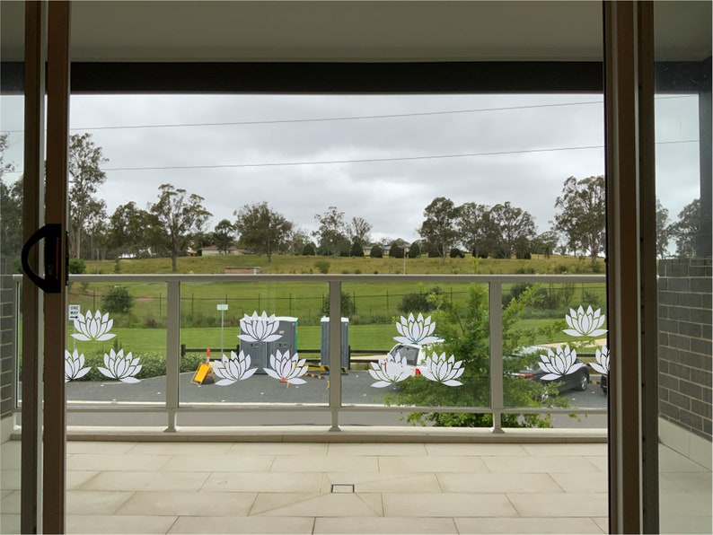 May include: A view from a balcony with a glass balustrade featuring white lotus flower decals. The balustrade overlooks a grassy field with trees in the background.