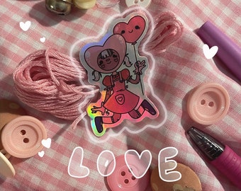 May include: A holographic sticker of a cartoon girl with pink hair and a pink dress holding a pink heart balloon. The sticker is on a pink and white gingham fabric with pink buttons, yarn, and pens.
