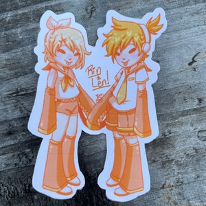 May include: A sticker featuring two anime characters, Rin and Len, with orange and yellow clothing. The text "Rin + Len!" is written in the center of the sticker.
