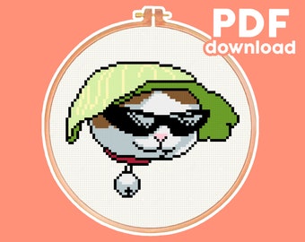 May include: Cross stitch pattern of a cat wearing sunglasses and a green hat. The cat is wearing a red collar with a bell. The pattern is in a hoop.